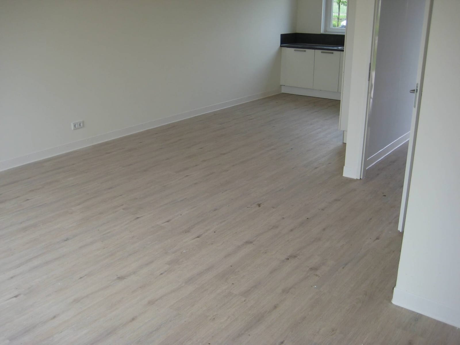 Lege nieuwbouwwoning met een lichte houtlook PVC-vloer en witte plinten