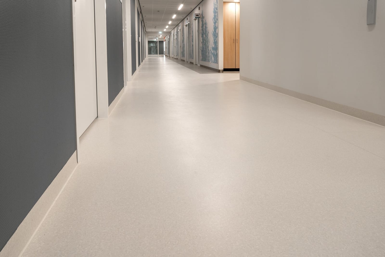 Lange, lichte gang in een nieuw ziekenhuis met een vloer die met een holle plint langs de wanden omhoog loopt