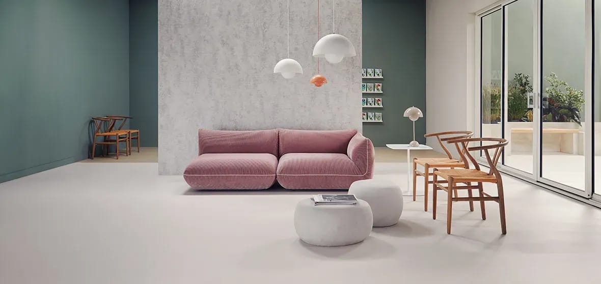 Lichte wachtruimte met een roze bank, poefs en houten stoelen op een egale lichtgrijze PVC-vloer