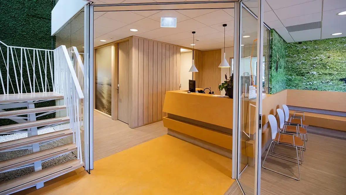 Balie en wachtruimte van een gezondheidscentrum met oranje marmoleum bij de entree en gestreept marmoleum onder de stoelen
