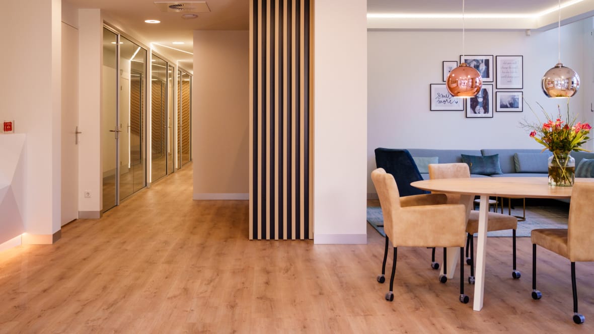 Wachtruimte en gang van een tandartspraktijk met een houtlook vinylvloer, een ovale tafel en stoelen