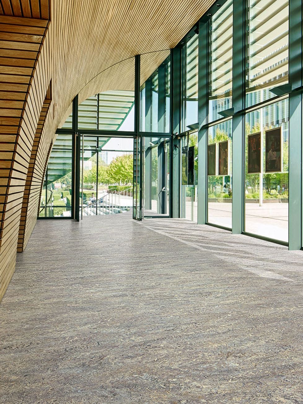 Lichte entreehal met glasgevel, houten lamellen en een grijs gemêleerde marmoleumvloer
