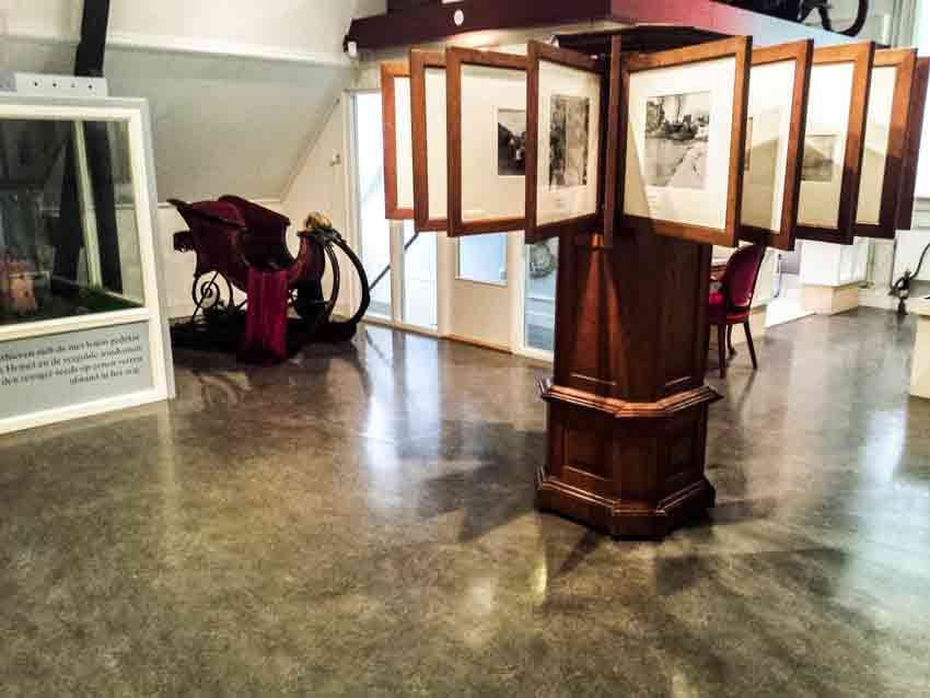 Expositieruimte in het Purmerends Museum met een arrenslee en een draaibaar fotopaneel op een donkere PVC-vloer