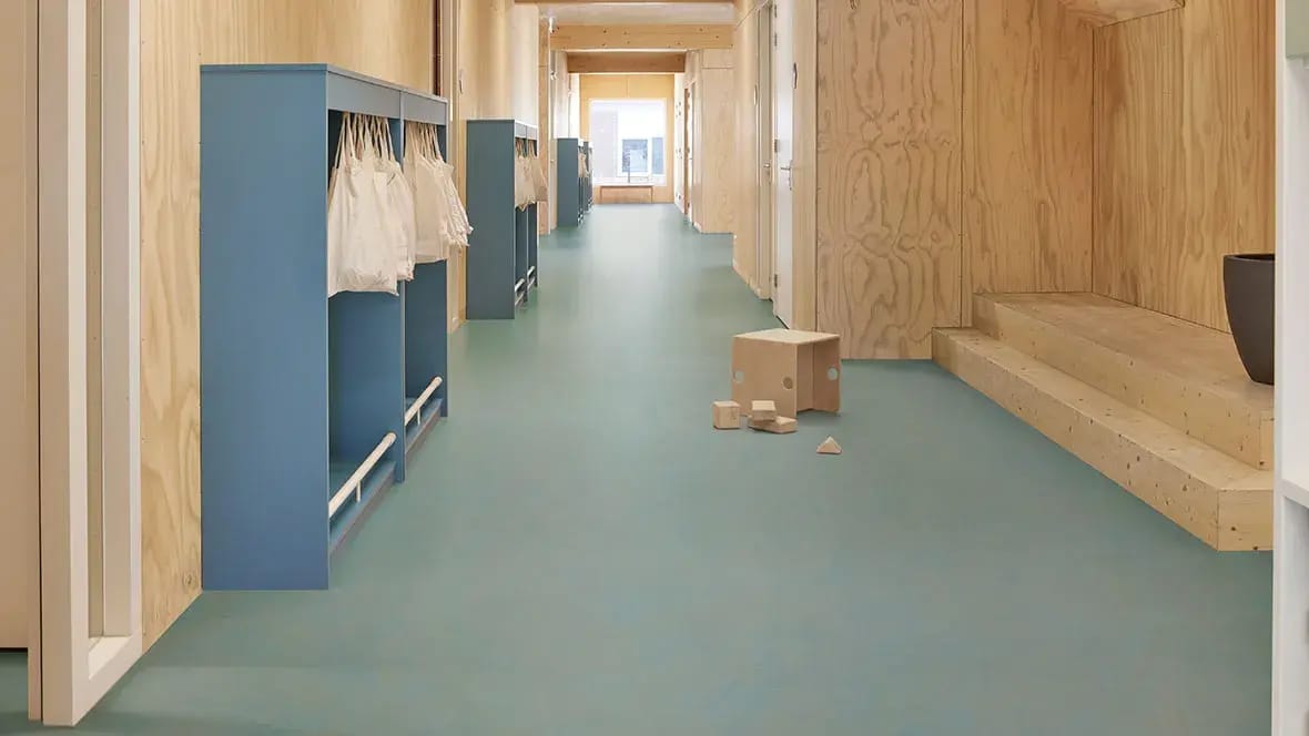 Gang met blauwe kapstokken en houten speelblokken op een blauwgroene marmoleumvloer
