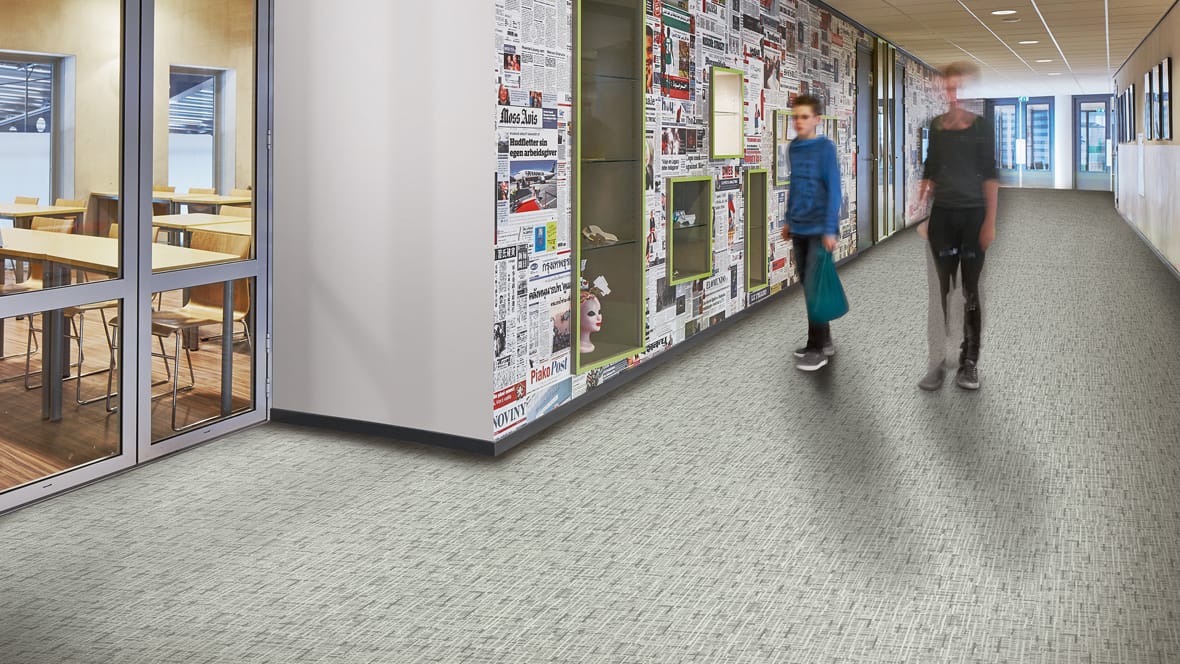 Schoolgang met twee lopende leerlingen langs een wand vol krantenpagina’s