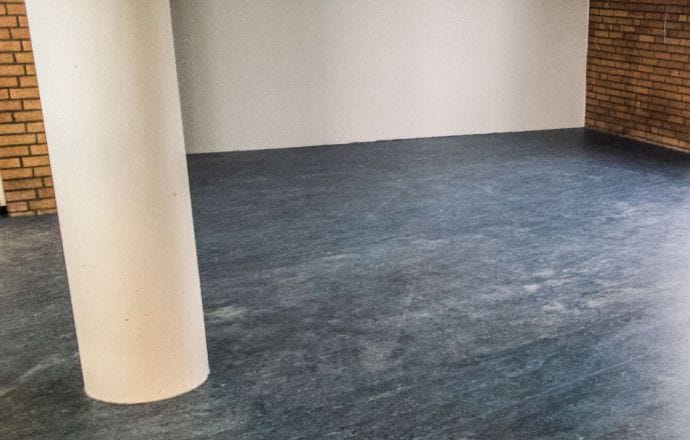 Ruimte in het gemaal in Wervershoof met een blauwgrijze marmoleumvloer, een witte kolom en een bakstenen wand