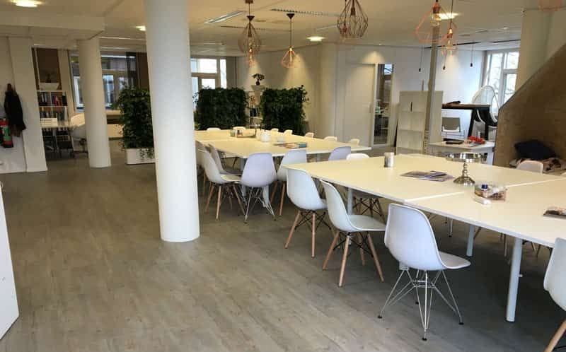 Open kantoorruimte met lange witte tafels en witte kuipstoelen op een lichte houtlook PVC-vloer