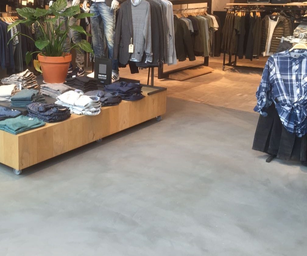 Herenmodezaak met een houten presentatietafel op een grijze naadloze betonlookvloer