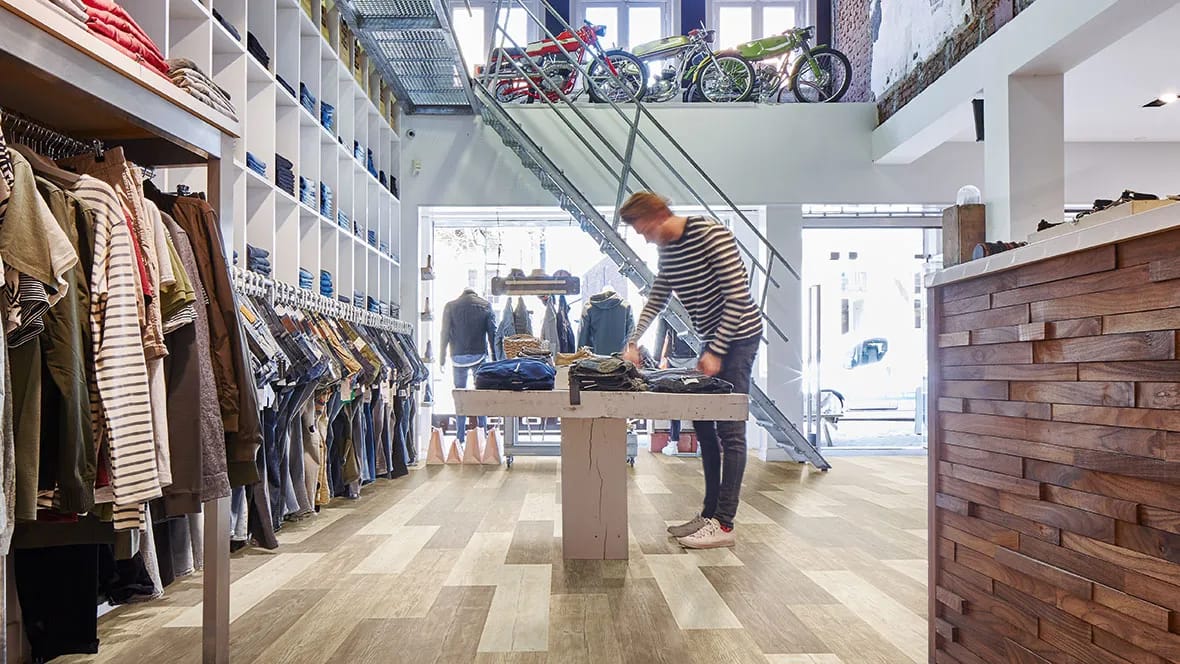 Kleine kledingwinkel met een verkoper aan een presentatietafel op een houtlook PVC-vloer