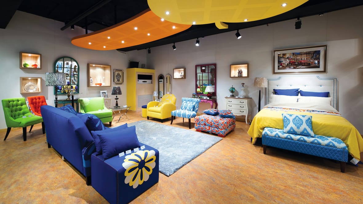 Meubelshowroom met kleurige banken, fauteuils en een tweepersoonsbed op een oranje marmoleumvloer