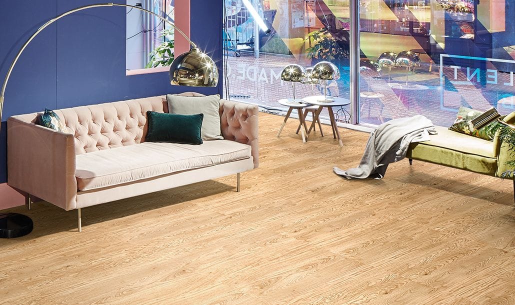 Zithoek met roze bank en groene chaise longue op een vloer in eikenlook, achter een glazen pui