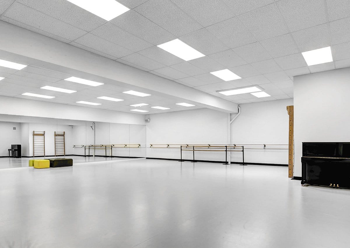 Lichte dansstudio met balletbarres, spiegelwand en piano op een grijze dansvloer