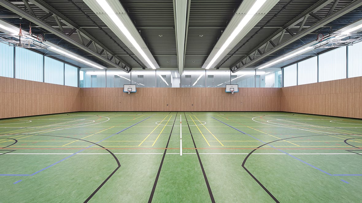 Sportzaal met houten wandbekleding en basketbalborden op een groene linoleum sportvloer met belijning