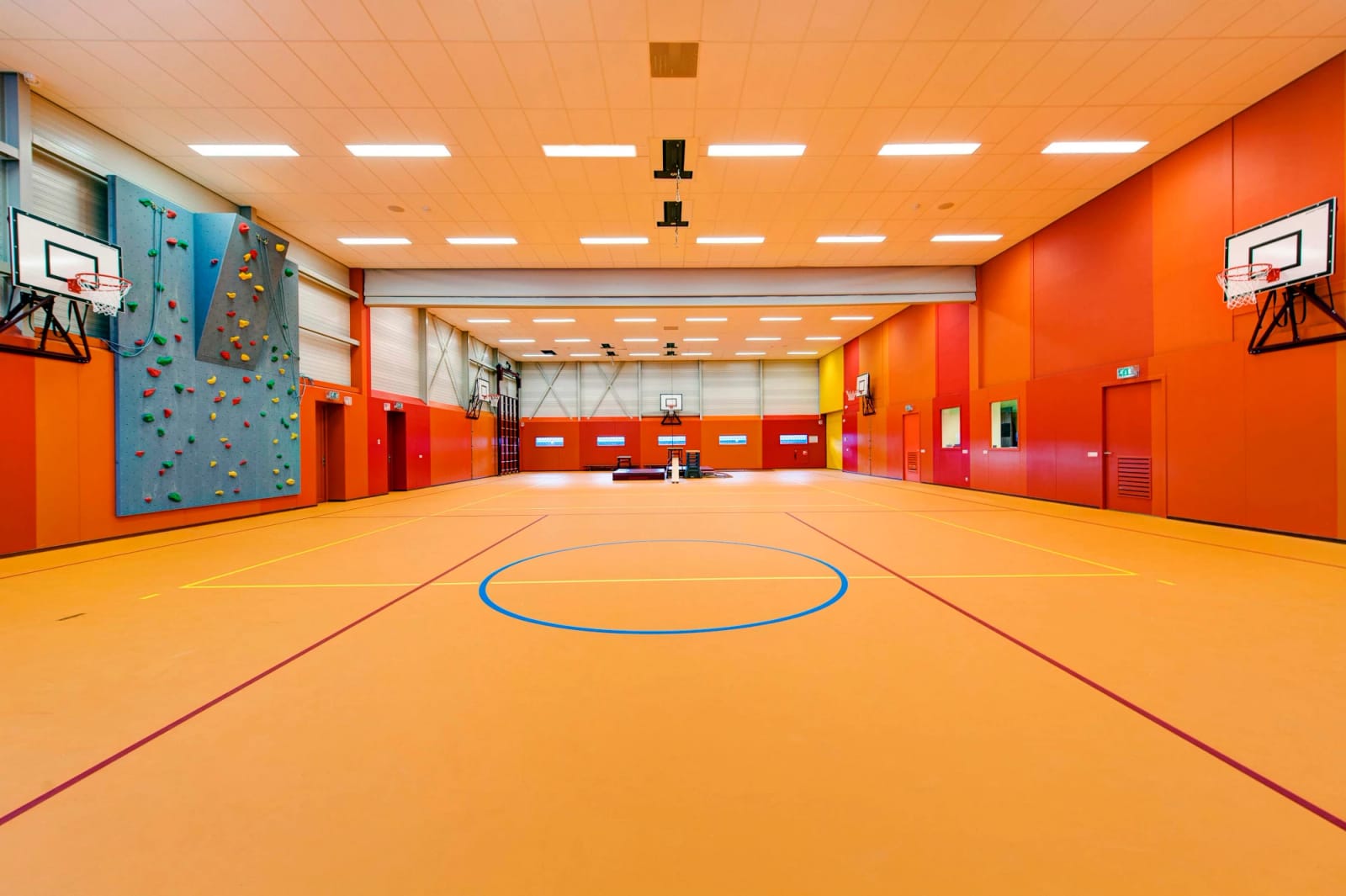 Sportzaal met een naadloze oranje sportvloer met belijning, een klimwand en basketbalborden