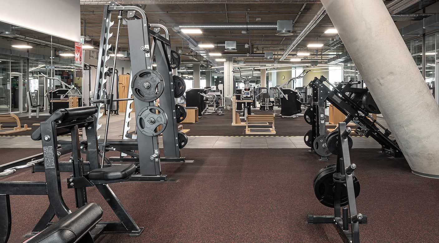 Grote fitnesszaal met krachttoestellen en halterschijven op een donkere, gespikkelde rubbervloer
