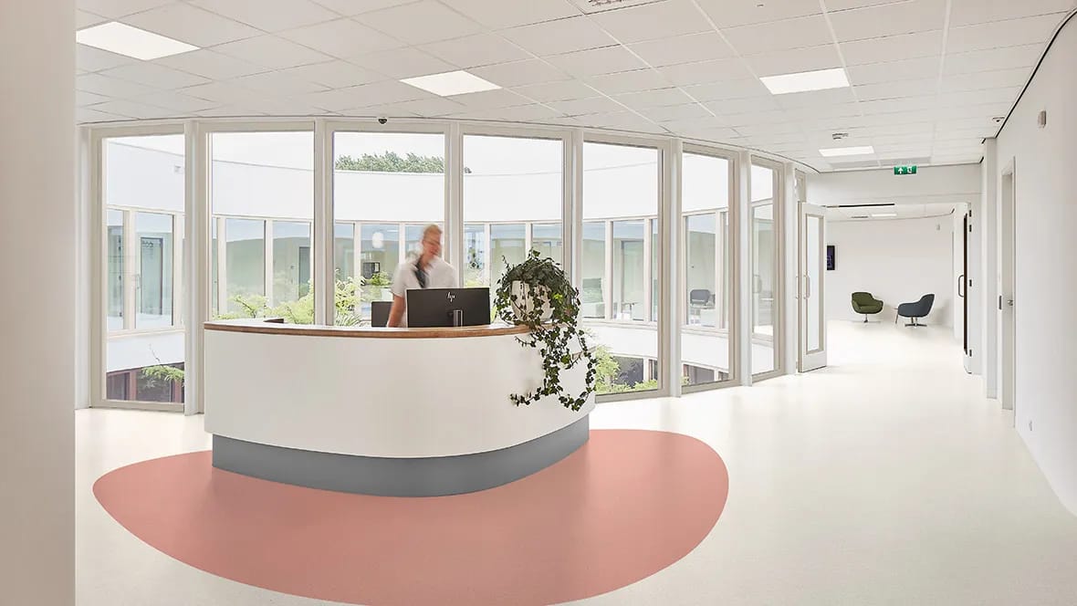 Lichte ontvangstbalie in een zorginstelling met een roze vloervlak rond de balie